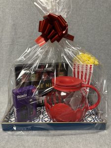 Image of the Movies basket which contains a Roku stick, a popcorn and popcorn seasonings assortment, a glass microwave popcorn popper, 4 popcorn serving containers and a blue and white lacquer serving tray.